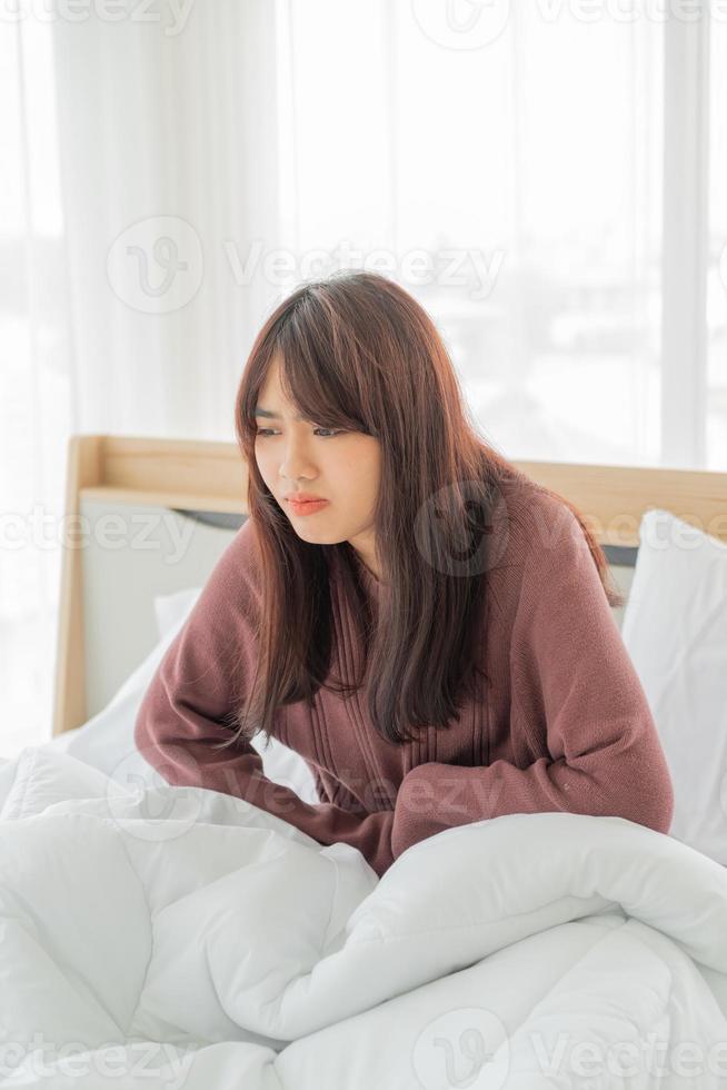 vacker asiatisk kvinna med magont och sover på sängen foto