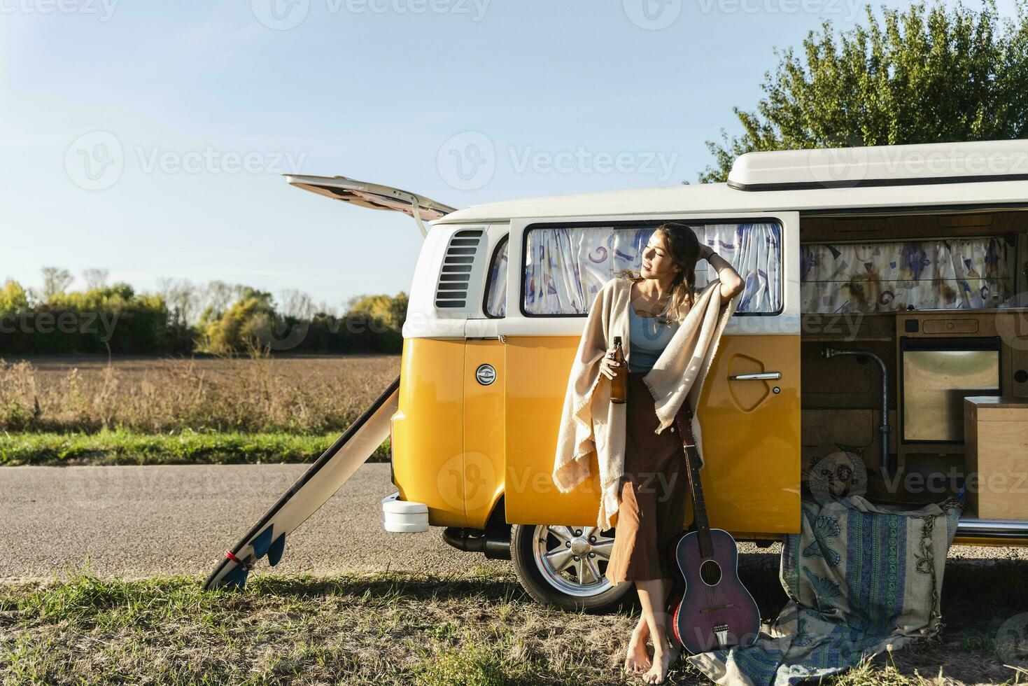 Söt kvinna på en väg resa med henne husbil, dricka öl, innehav gitarr foto