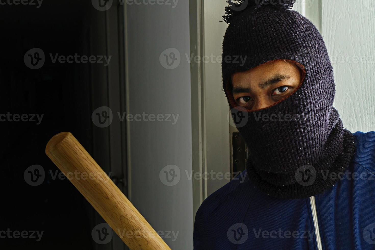 maskerad rånare med basebollträ gömmer sig bakom dörren foto