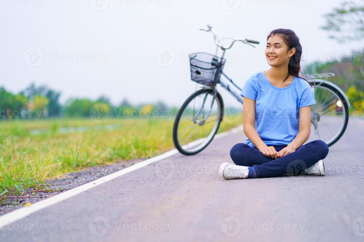 flicka med cykel, kvinna som sitter på vägen i parken och en cykel foto