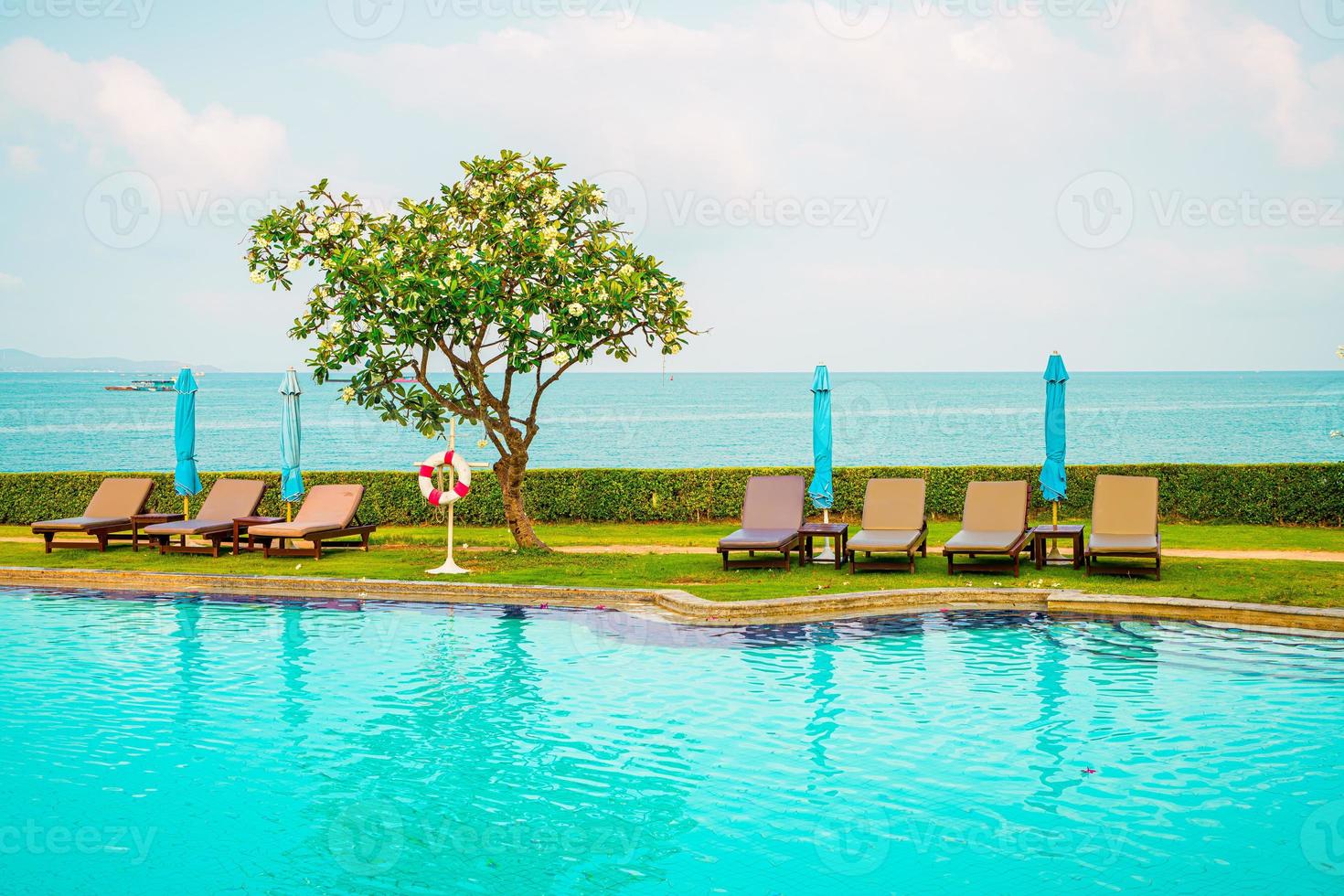 stol pool och paraply runt poolen med havet havet bakgrund foto