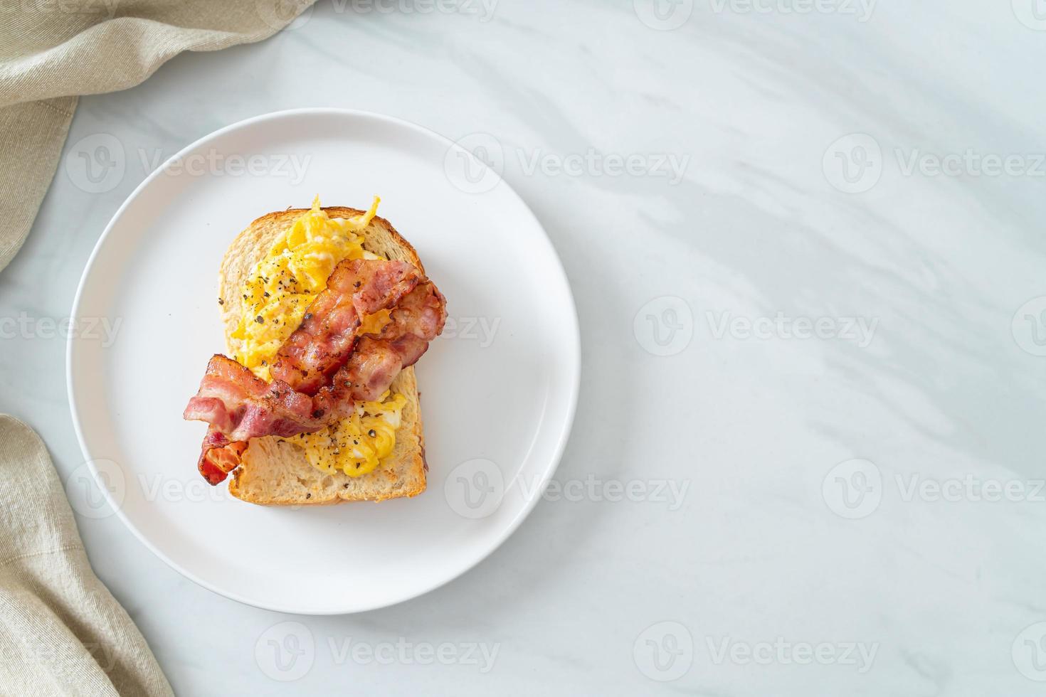 brödskål med äggröra och bacon på den vita plattan foto