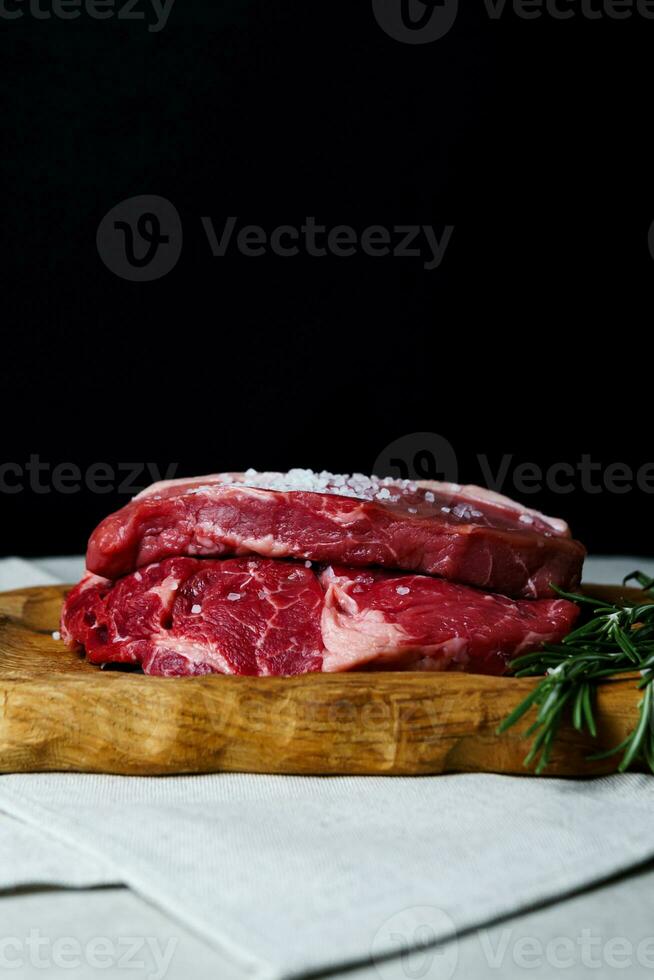 rå organisk nötkött kött med rosmarin, kryddor, salt och röd peppar på trä- skärande styrelse foto
