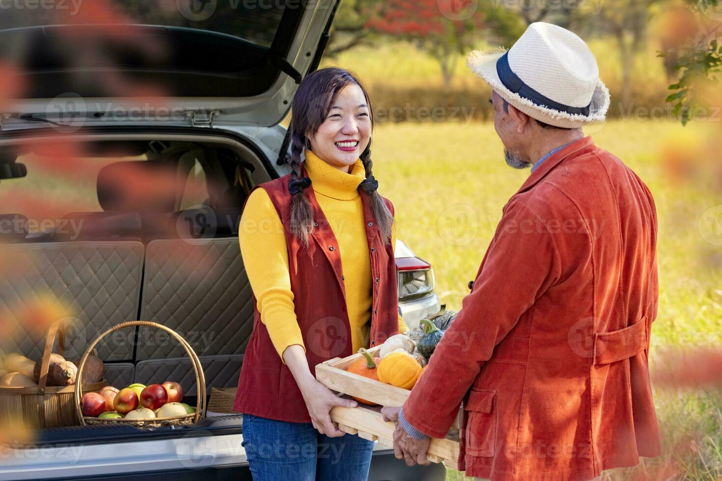 Lycklig jordbrukare familj bärande organiska ämnen hemodlade producera skörda med äpple, squash och pumpa medan försäljning på bil trunk i lokal- marknadsföra med falla Färg från lönn träd under höst säsong foto