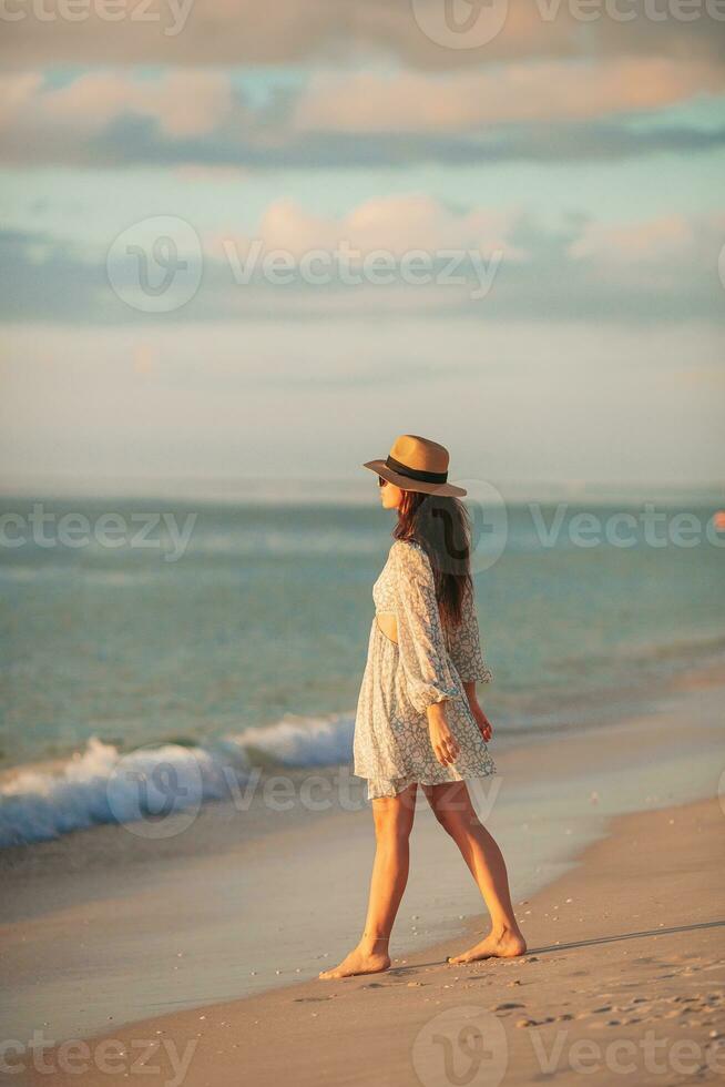 ung skön kvinna på sugrör hatt på de strand på solnedgång foto