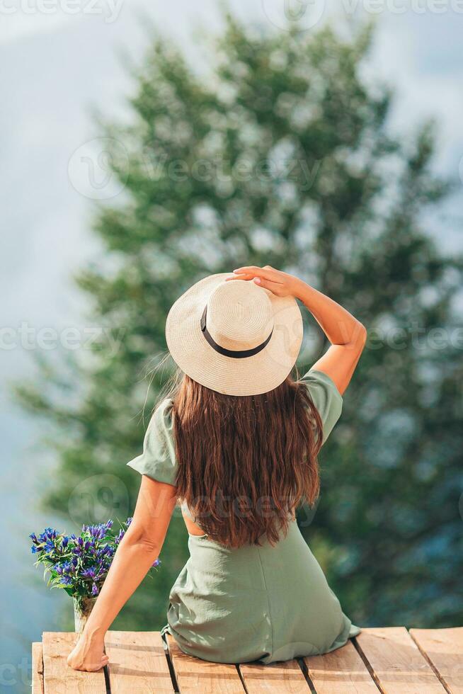 tillbaka se av ung kvinna sitta på en terrass på en höjd i de bergen mot de bakgrund av dimma och bergen foto