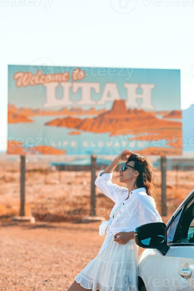 skön kvinna på henne resa förbi de bil på de bakgrund av Välkommen till utah stat gräns tecken rätt i de monument dal foto