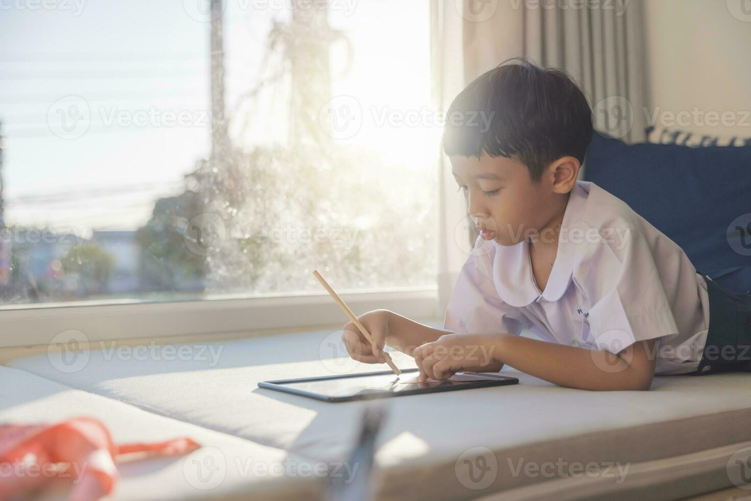 Lycklig asiatisk pojke 6-7 år gammal, svart hår, vit hud, bär vit skjorta och blå shorts skrivning på en svarta tavlan. barn i skola uniformer av thailand. begrepp handla om utbildning, spela, kreativitet. foto