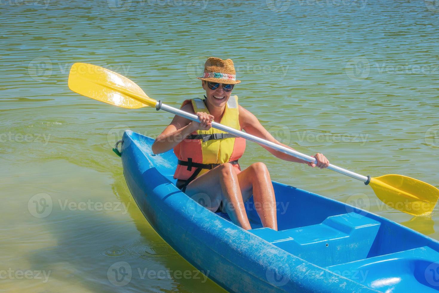 le kvinna i flytväst som paddlar en kanot på floden foto