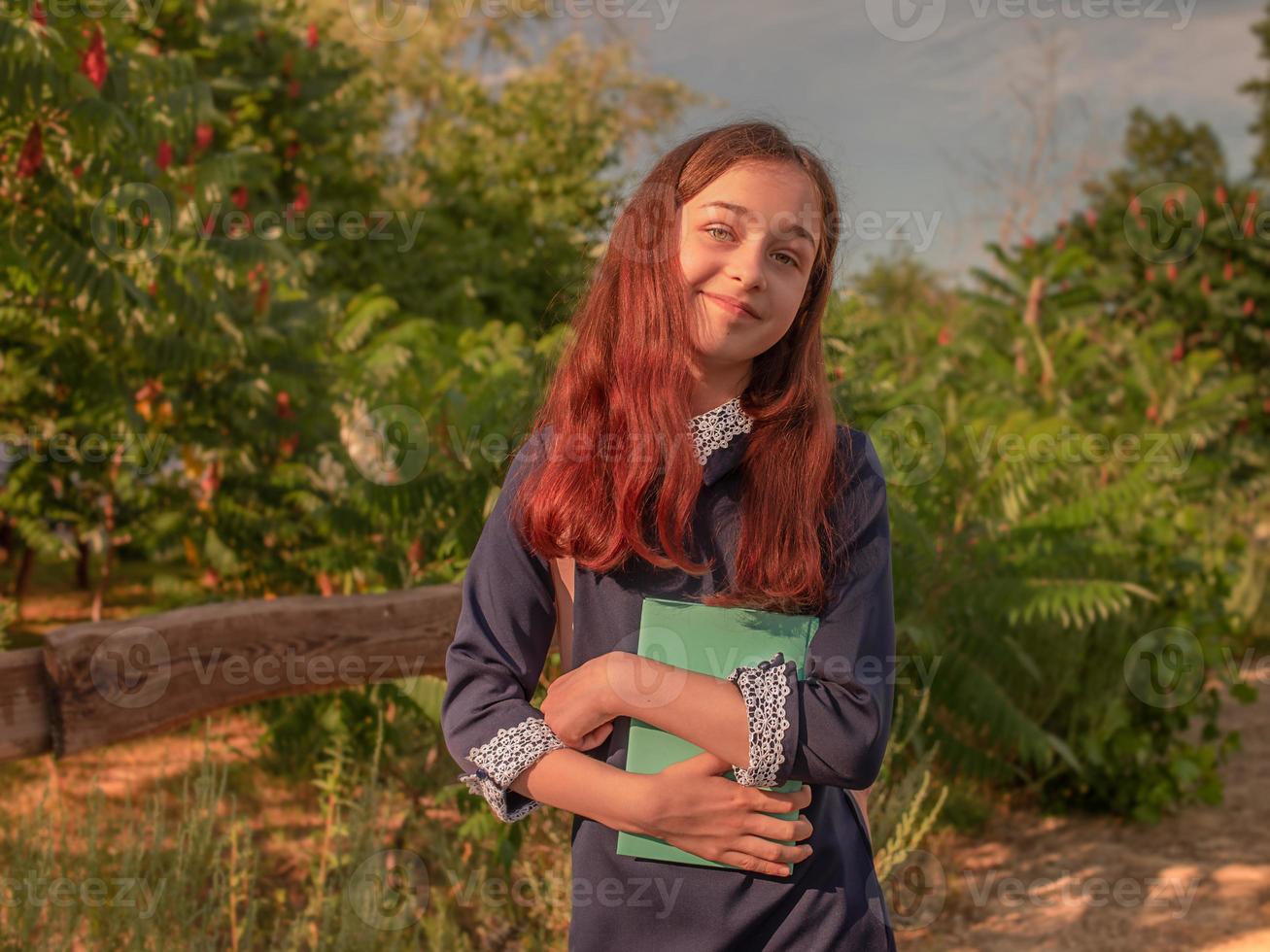 skolflicka i en skolklänning med en anteckningsbok och en ryggsäck utomhus foto