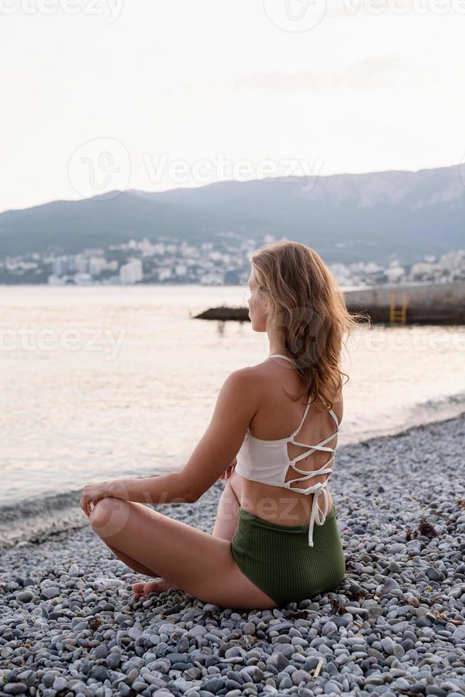 ung kvinna som mediterar på stranden foto