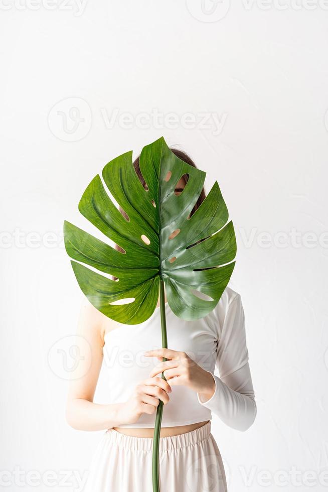 glad vacker kvinna i mysiga kläder som håller ett grönt monstera blad foto