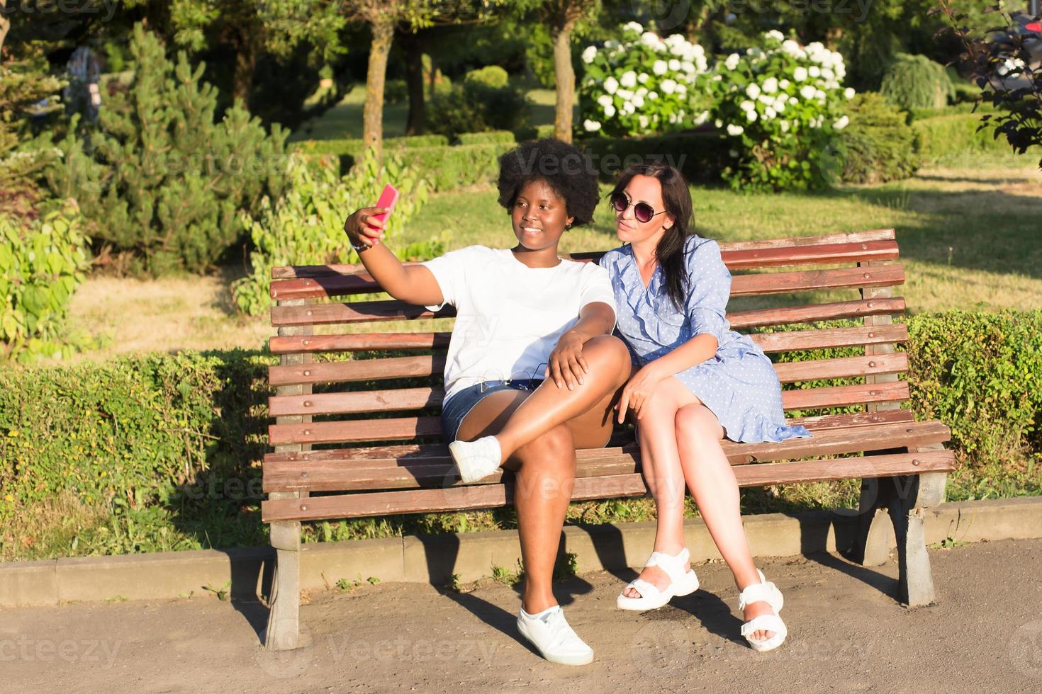 glada tjejer av olika nationaliteter tar selfies på sommaren foto