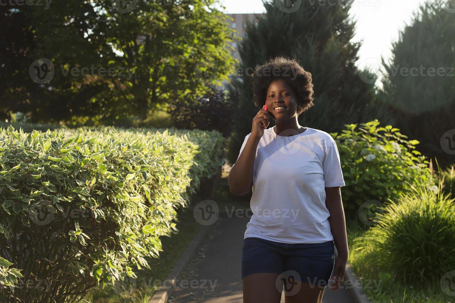 glad afroamerikansk kvinna med en telefon på gatan på sommaren foto