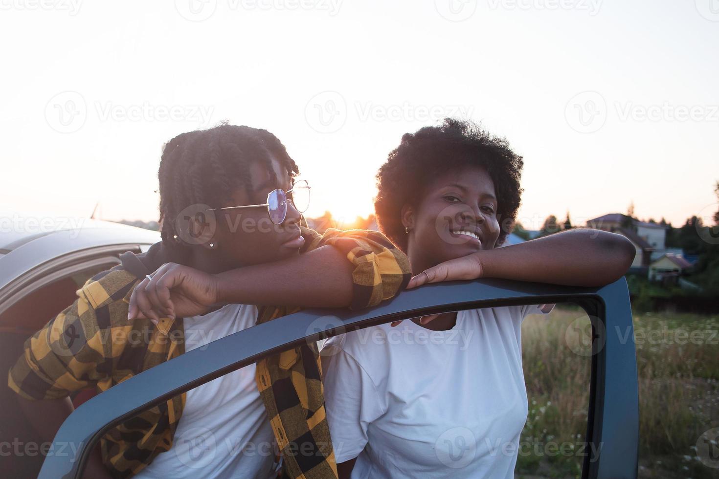 två glada afroamerikanska kvinnor nära bilen vid solnedgången, livsstil foto