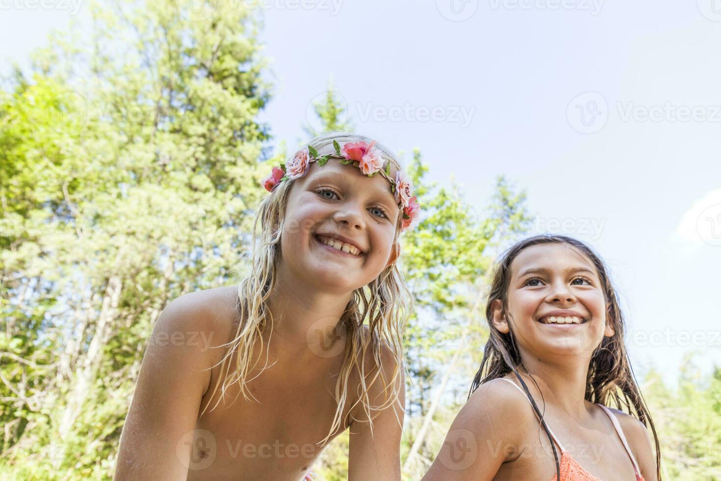 porträtt av Lycklig flicka bär blomma krona och vän utomhus i sommar foto