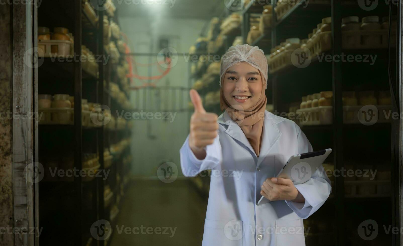porträtt av ung asiatisk muslim kvinna forskare håller på med forskning på en svamp fabrik, granskning svamp surdeg ombud i en steril och temperaturkontrollerad rum. foto