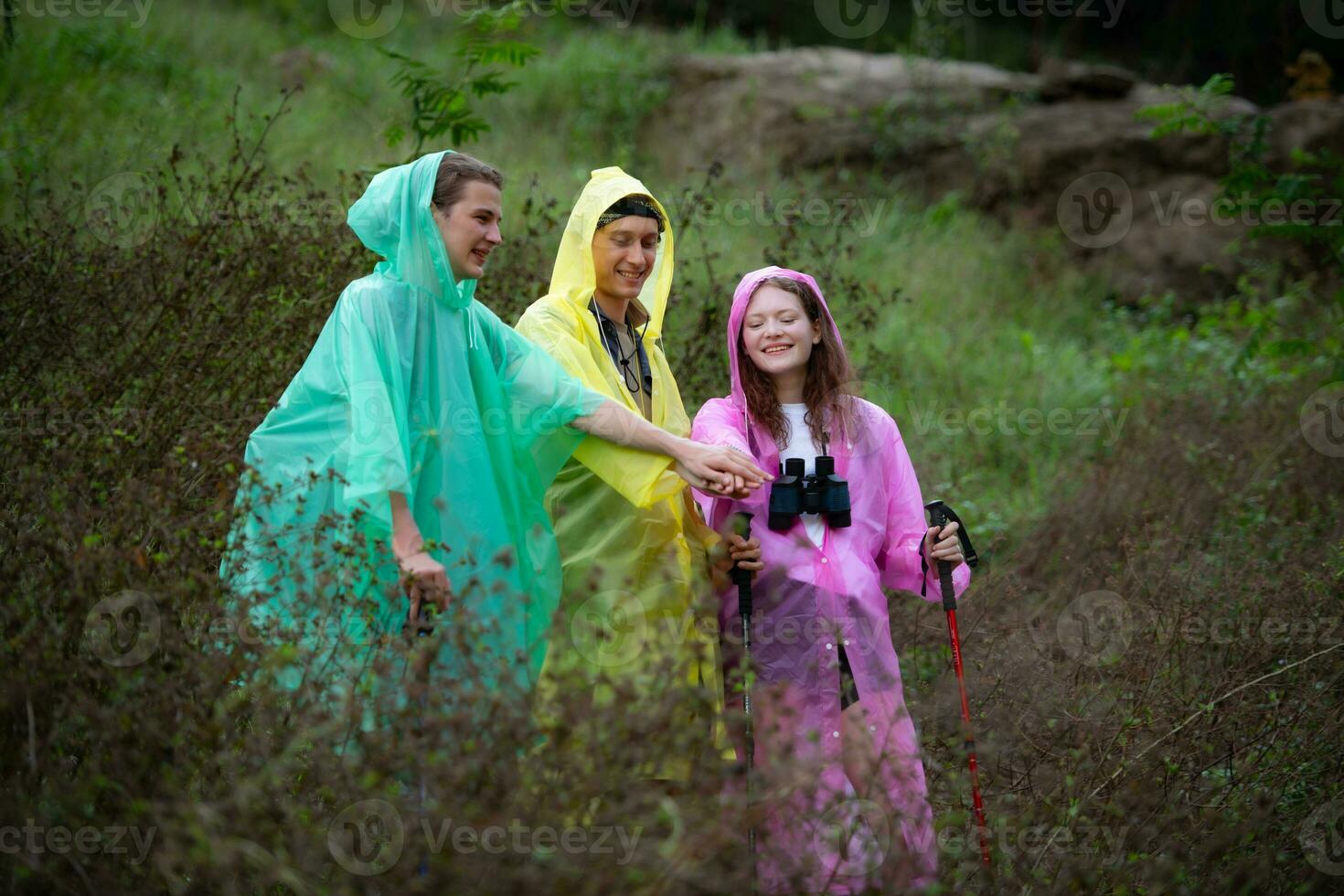 grupp av vänner i regnrockar med ryggsäckar på en vandra i de skog, förbereda till vandring efter de regn har stannade. foto