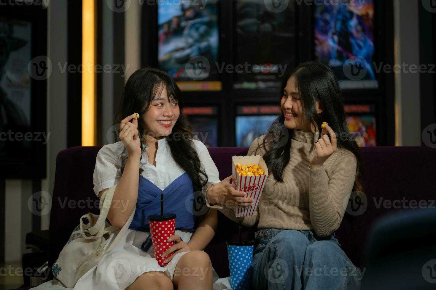 två ung asiatisk kvinnor äter popcorn och väntar för tittar på film på främre av bio foto