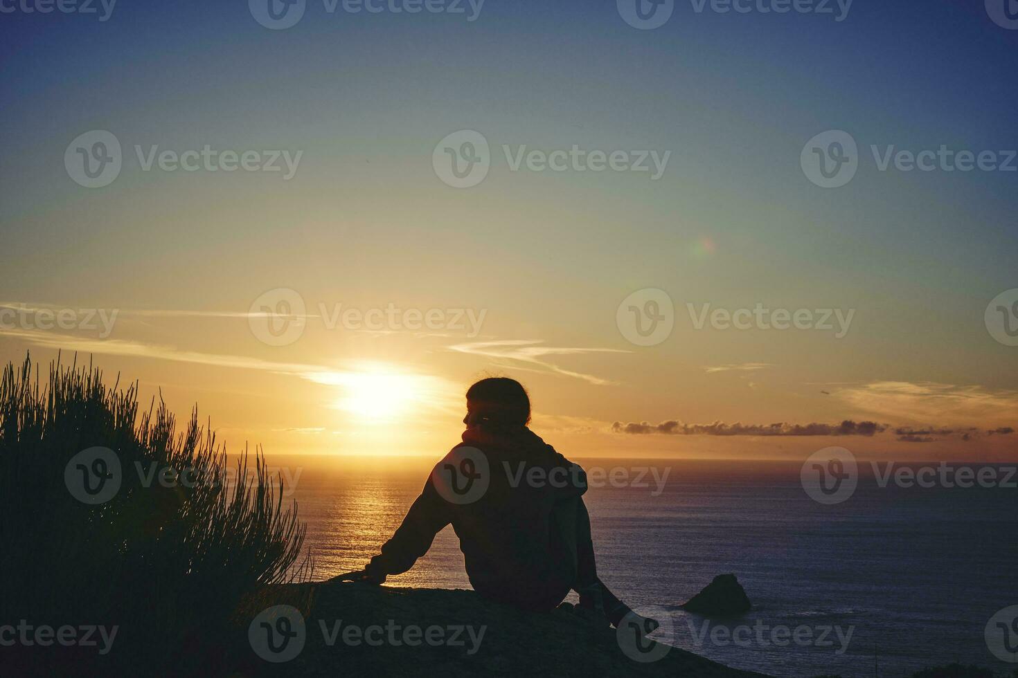 silhuett av en ung kvinna på henne tillbaka på de topp av en klippa tittar på en solnedgång. foto
