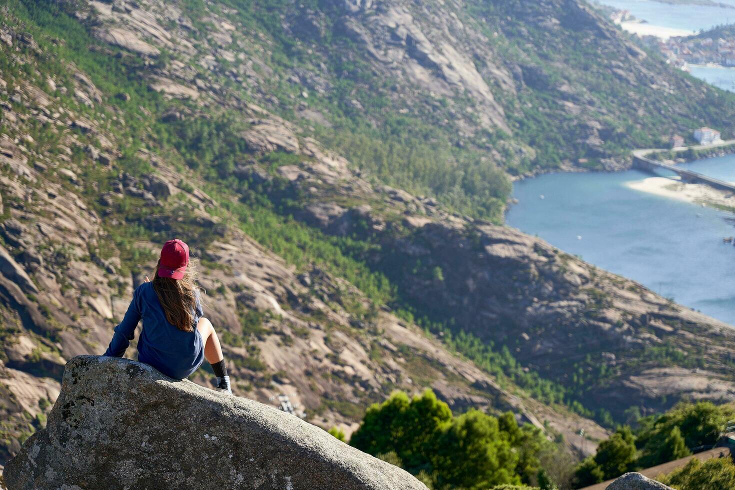 flicka med röd keps är på en sten på de topp av de berg utsikt de atlanten kust. foto