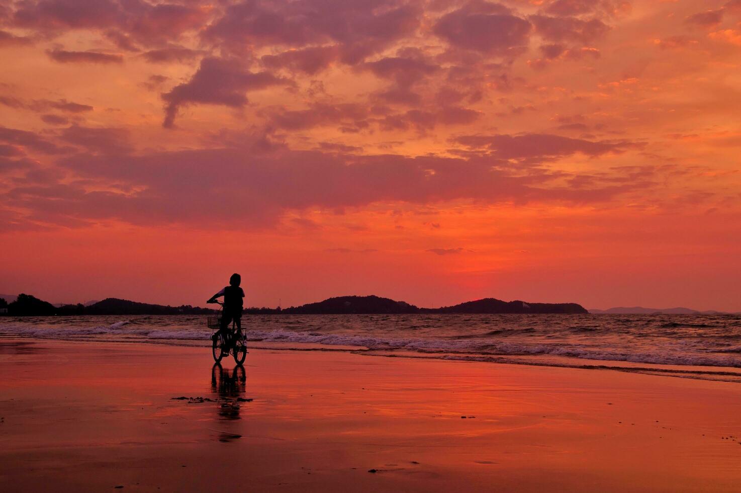 silhuett av pojke ridning en cykel på de strand med dramatiskt himmel foto