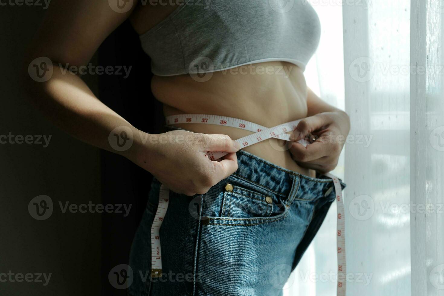 stänga upp av en mage med ärr från c-sektion och abdominal fett. kvinnors hälsa. en kvinna klädd upp i sportkläder demonstrera henne ofullständig kropp efter en förlossning med barnkammare på de bakgrund. foto