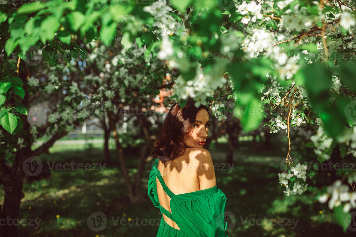 en ung flicka står i parken under ett blommande äppelträd foto