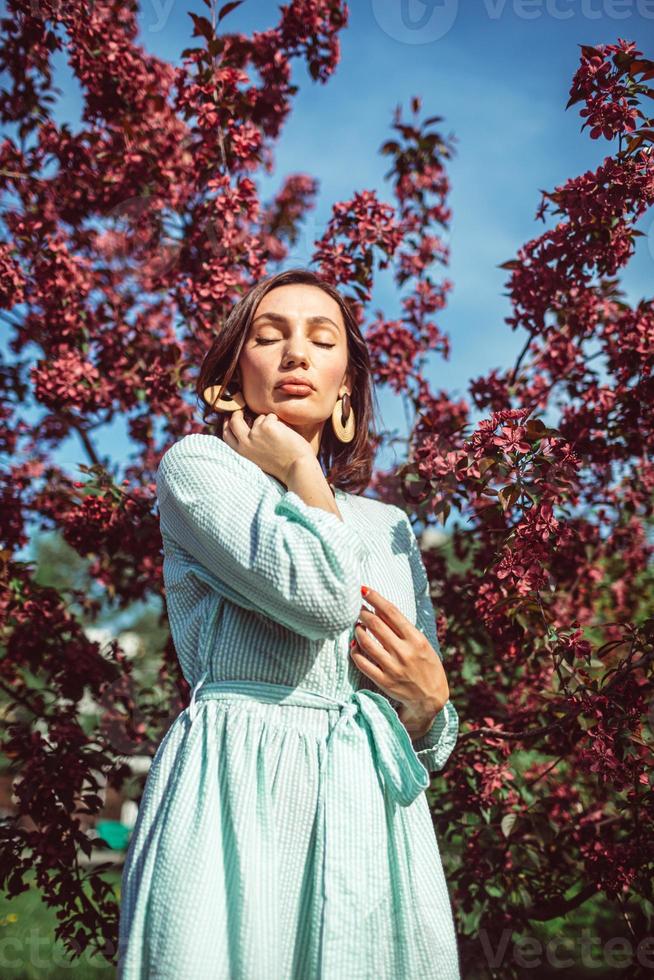 en ung flicka står i parken under ett blommande äppelträd foto