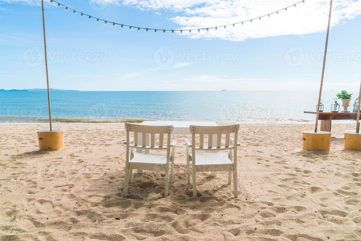 vita stolar och bord på stranden med utsikt över blått hav och klar himmel foto
