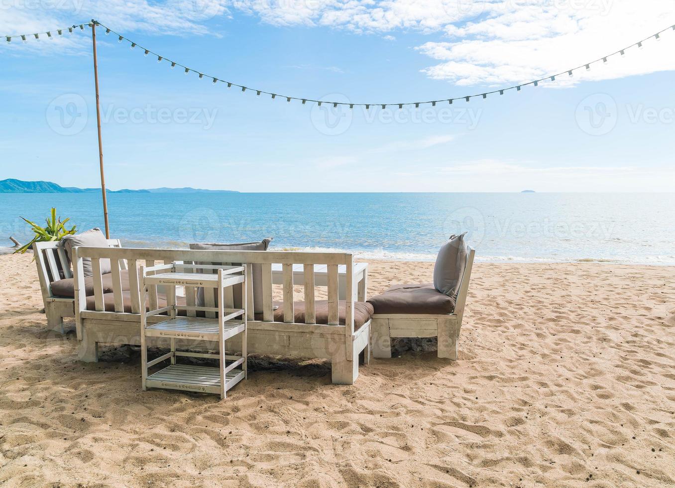 vita stolar och bord på stranden med utsikt över blått hav och klar himmel foto