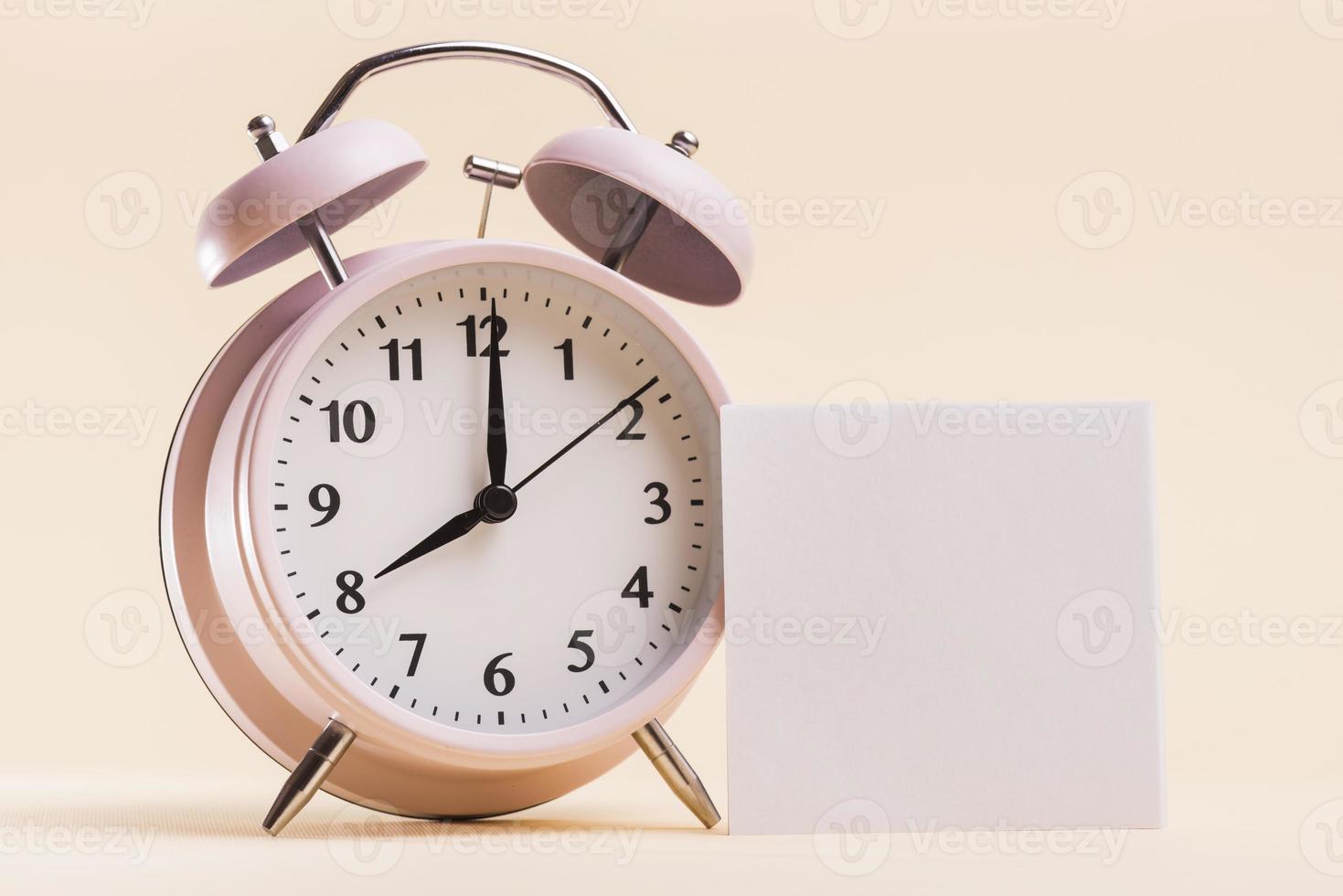 rosa väckarklocka med tom vit självhäftande anteckning beige bakgrund. foto