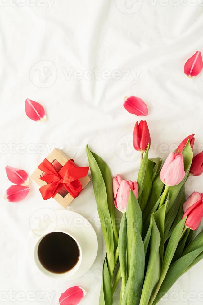 rosa tulpaner, kaffekopp och gåva ovanifrån på vit säng foto