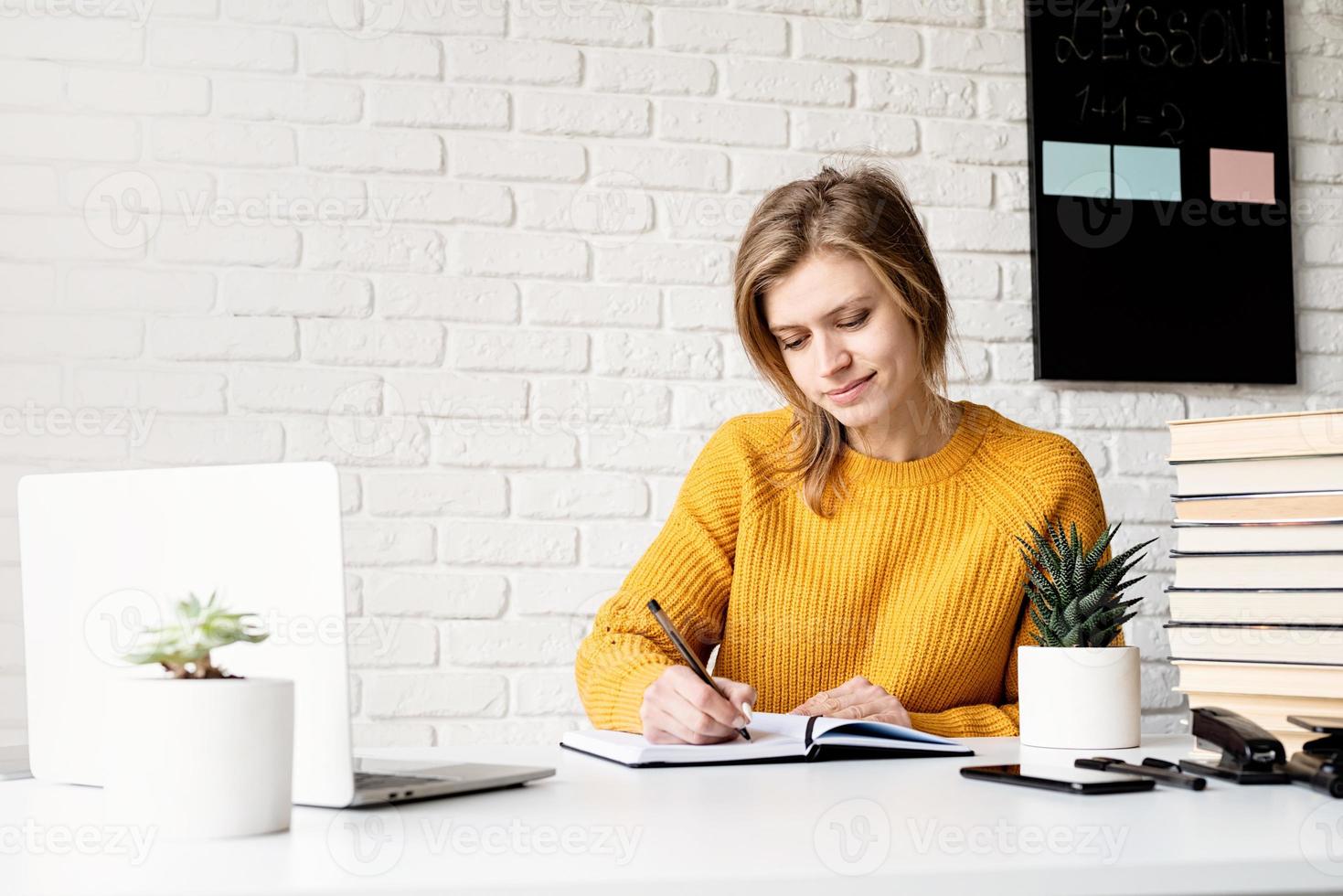 kvinna i tröja som studerar online med hjälp av bärbar datorhandstil i anteckningsboken foto