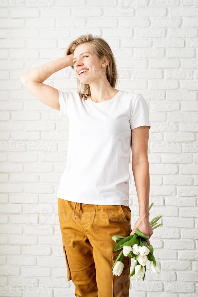 ung kvinna som bär tomma vita t-shirtinnehav tulpanblommor foto