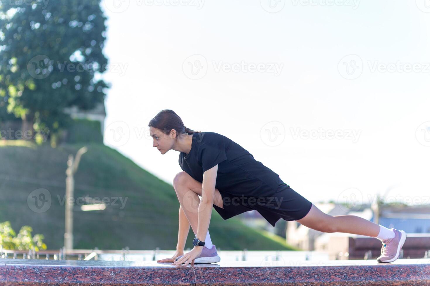 ung, passa och sportig flicka i svart kläder stretching efter de träna nära de offentlig fontän i de urban stad parkera. foto