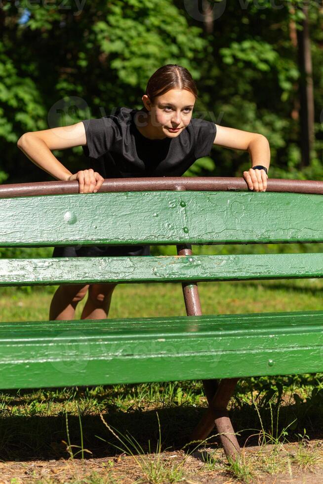 skön ung sportig kvinna i svart t-shirt, svart shorts och rosa utbildare uppvärmningen upp utövar triceps och bröst foto