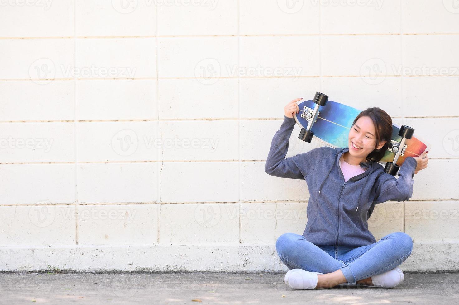 asiatisk kvinna med surfskatesammanträde mot betongväggen foto