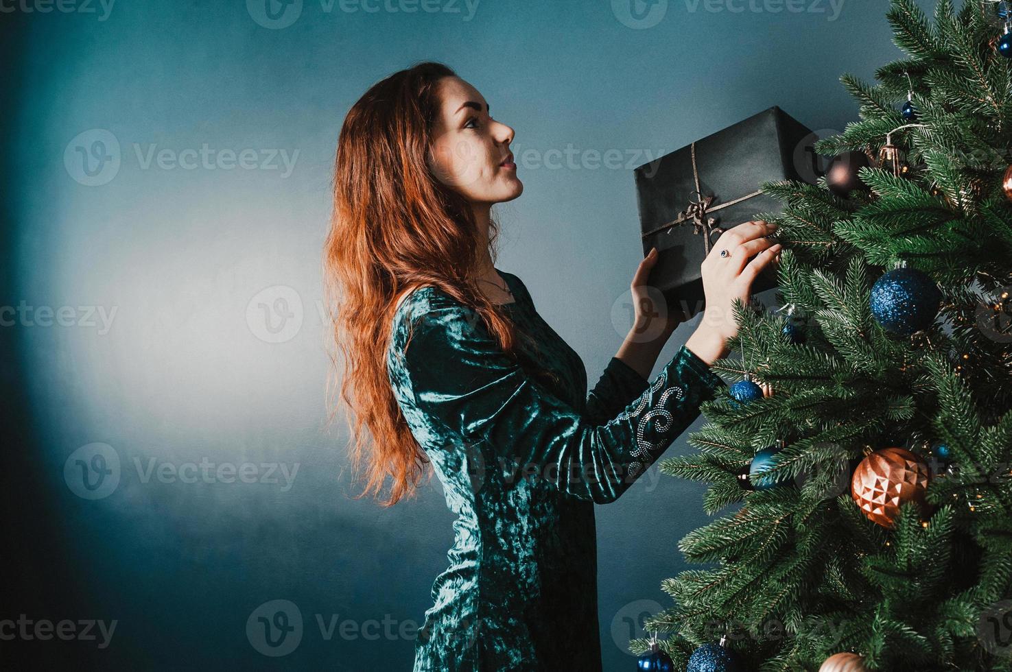 vacker kvinna som dekorerar julgranen som rymmer en presentask foto