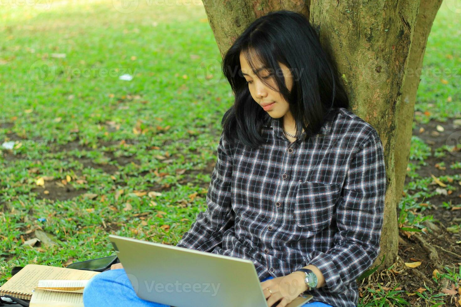 porträtt av fokuserade ung asiatisk kvinna surfing internet använder sig av bärbar dator till arbetssätt avlägset, läsa bok, och skrivning i anteckningsbok. attraktiv asiatisk studerande studie i utomhus foto