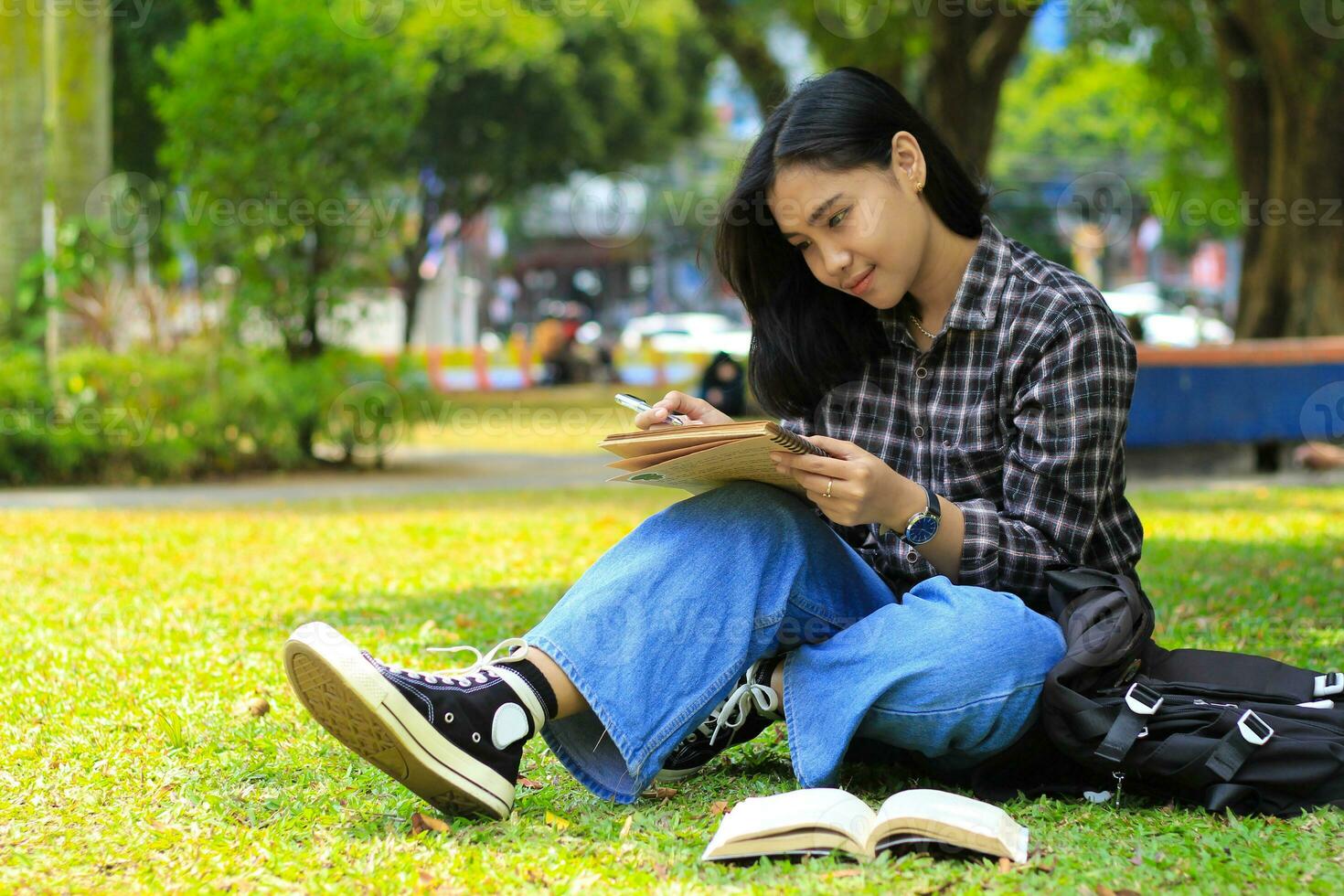 leende asiatisk skön ung kvinna njut av skrivning till do lista och aning i anteckningsbok i utomhus stad parkera foto