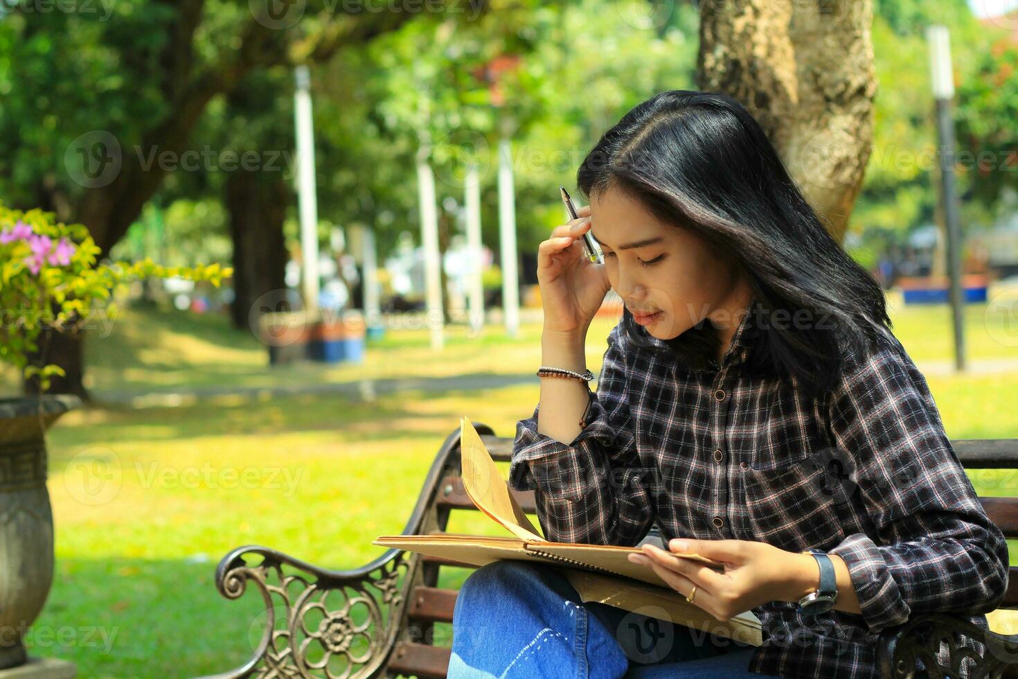 förvirrande asiatisk ung kvinna tänkande ett aning och skrivning i anteckningsbok med en penna i natur utomhus område foto