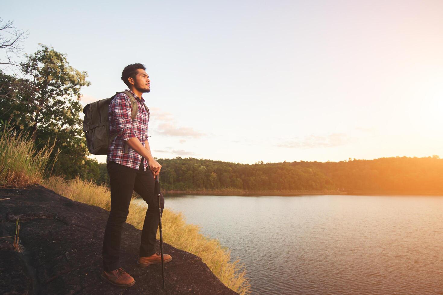 hipster vandrare man står på berget och njuter av solnedgången över sjön. foto