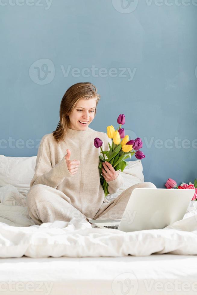 kvinna på sängen med hjälp av bärbar dator visar tummen oss foto