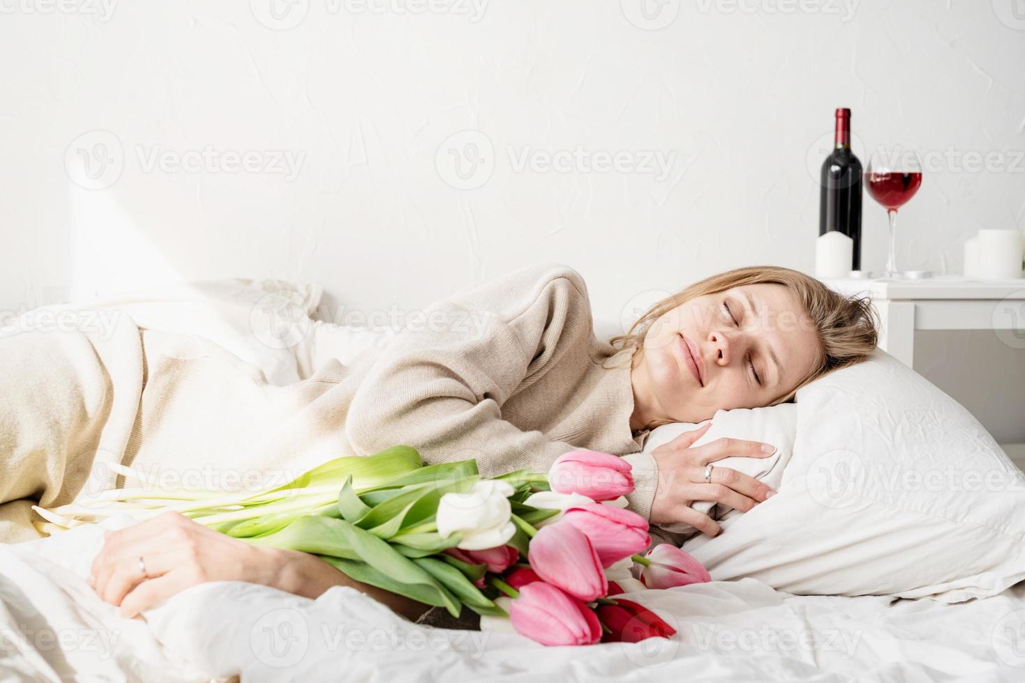 kvinna som ligger i sängen som bär pyjamas som rymmer buketten för tulpanblommor foto