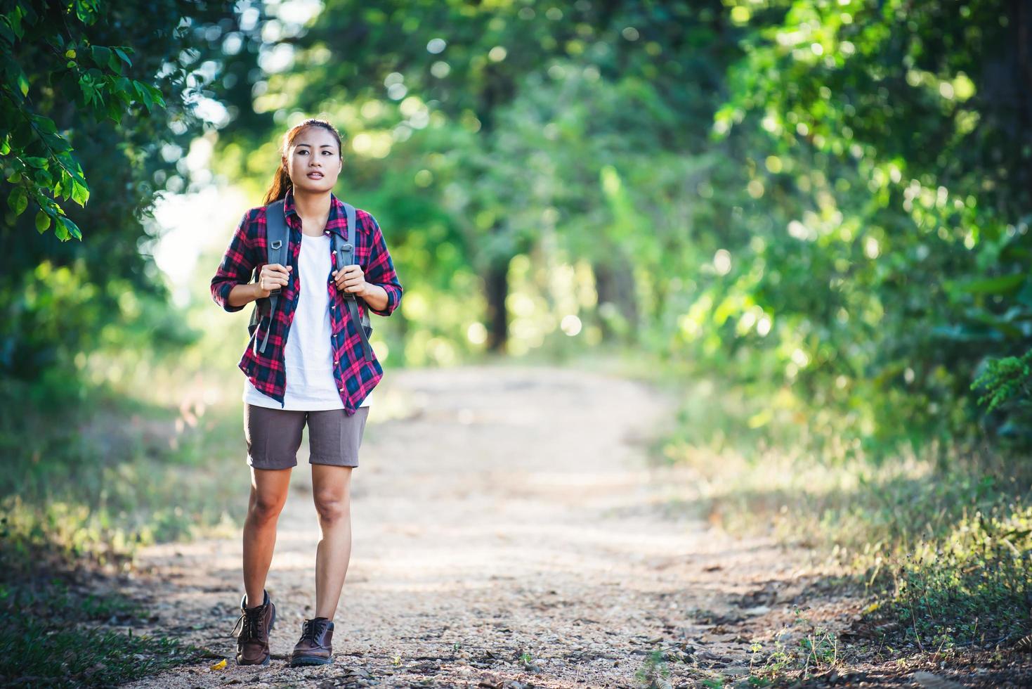 ung kvinna vandrare med ryggsäck promenader och ler på en lant spår foto