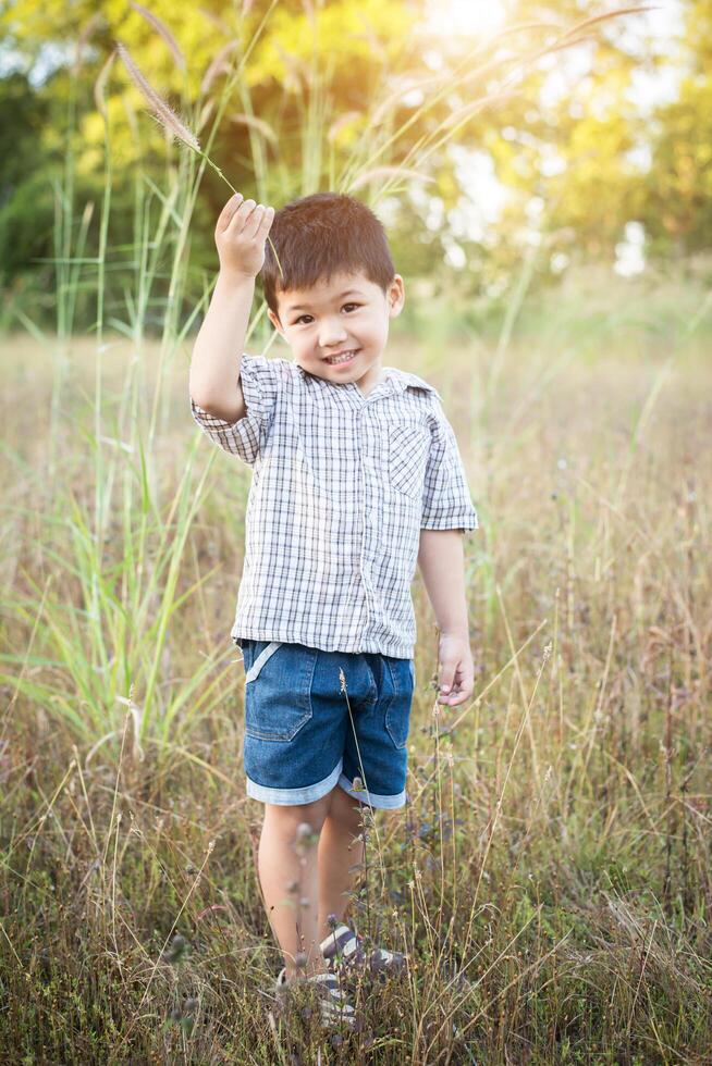 glad liten asiatisk pojke som leker utomhus. söt asiatisk pojke på fältet. foto