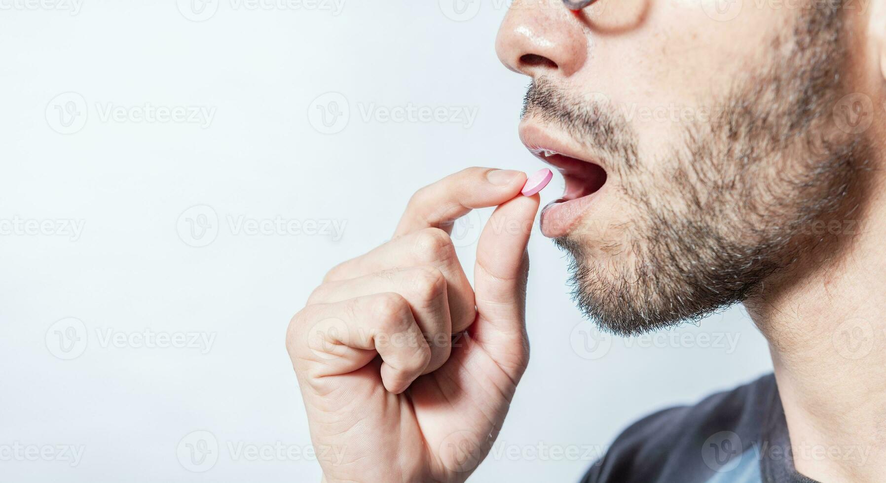 närbild av en man tar ett aspirin. person tar en piller isolerat, stänga upp av ung man sätta en piller i hans mun. självmedicinering begrepp, man sätta en piller i hans mun isolerat foto
