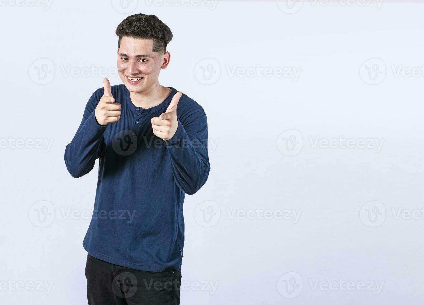 ung man med tummen upp på vit bakgrund, positiv pojke med tummen upp håller på med ok, leende man som visar ok gest ser på kamera foto