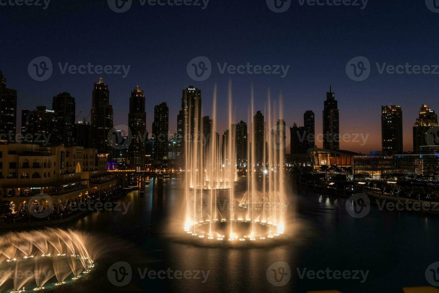 dubai sång fontäner på natt sjö se mellan skyskrapor. stad horisont i skymning modern arkitektur i uae huvudstad stadens centrum. foto